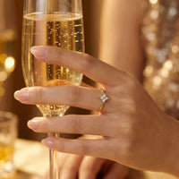Thumbnail for Crystal Flower Ring worn on a hand holding a champagne flute, featuring a tiny crystal flower and delicate band by Brother & Sisters.
