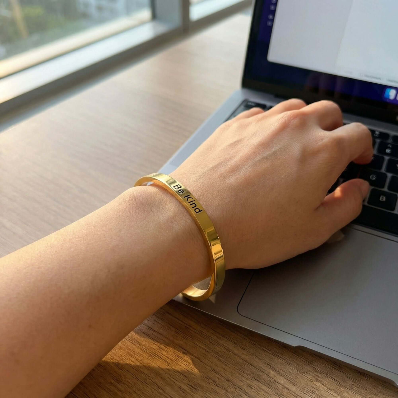 Matching Couple Bracelet with engraved "Be Kind" worn on wrist next to laptop, by Brother & Sisters.