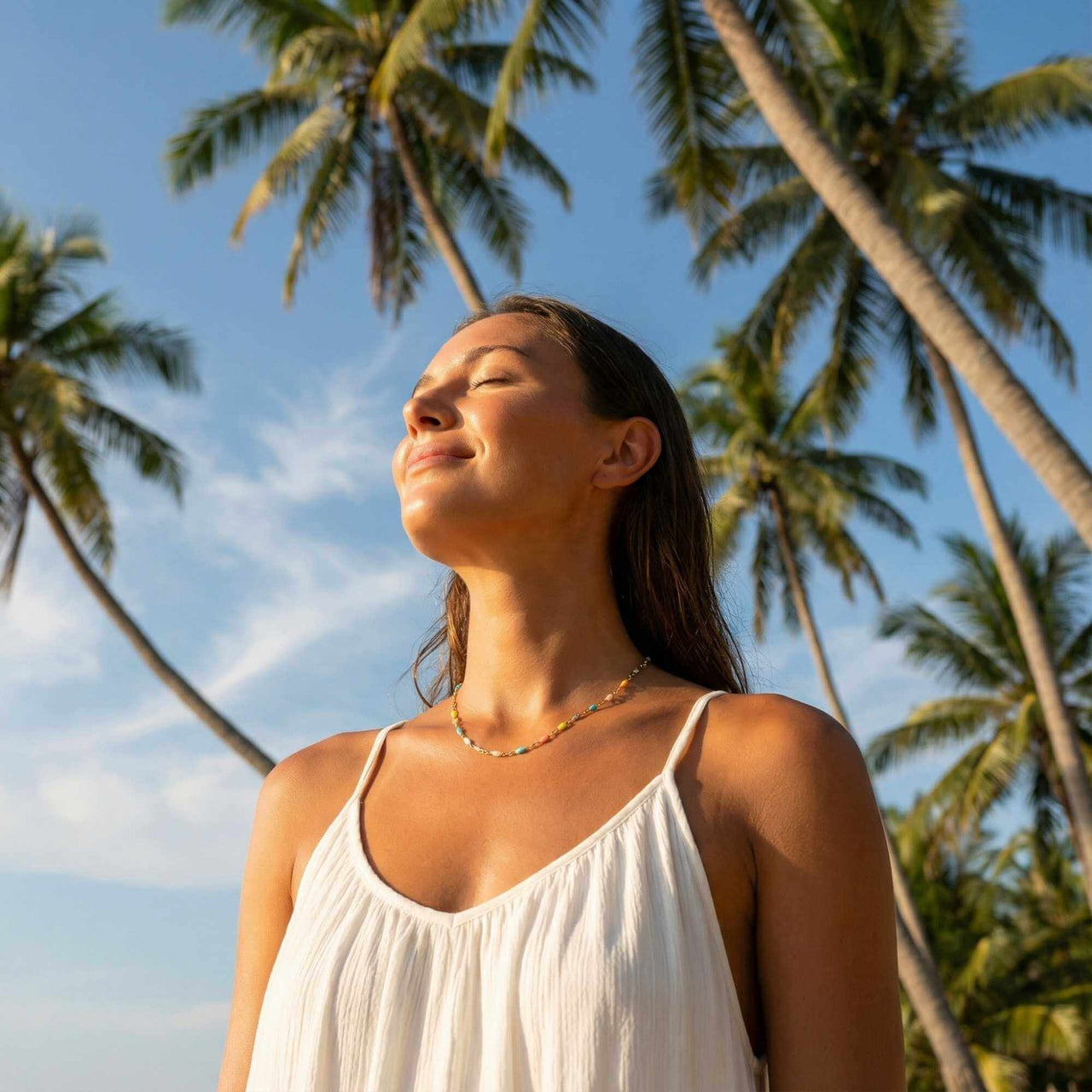 Woman wearing a Rainbow Choker by Brother & Sisters under palm trees, enjoying sunny outdoors.