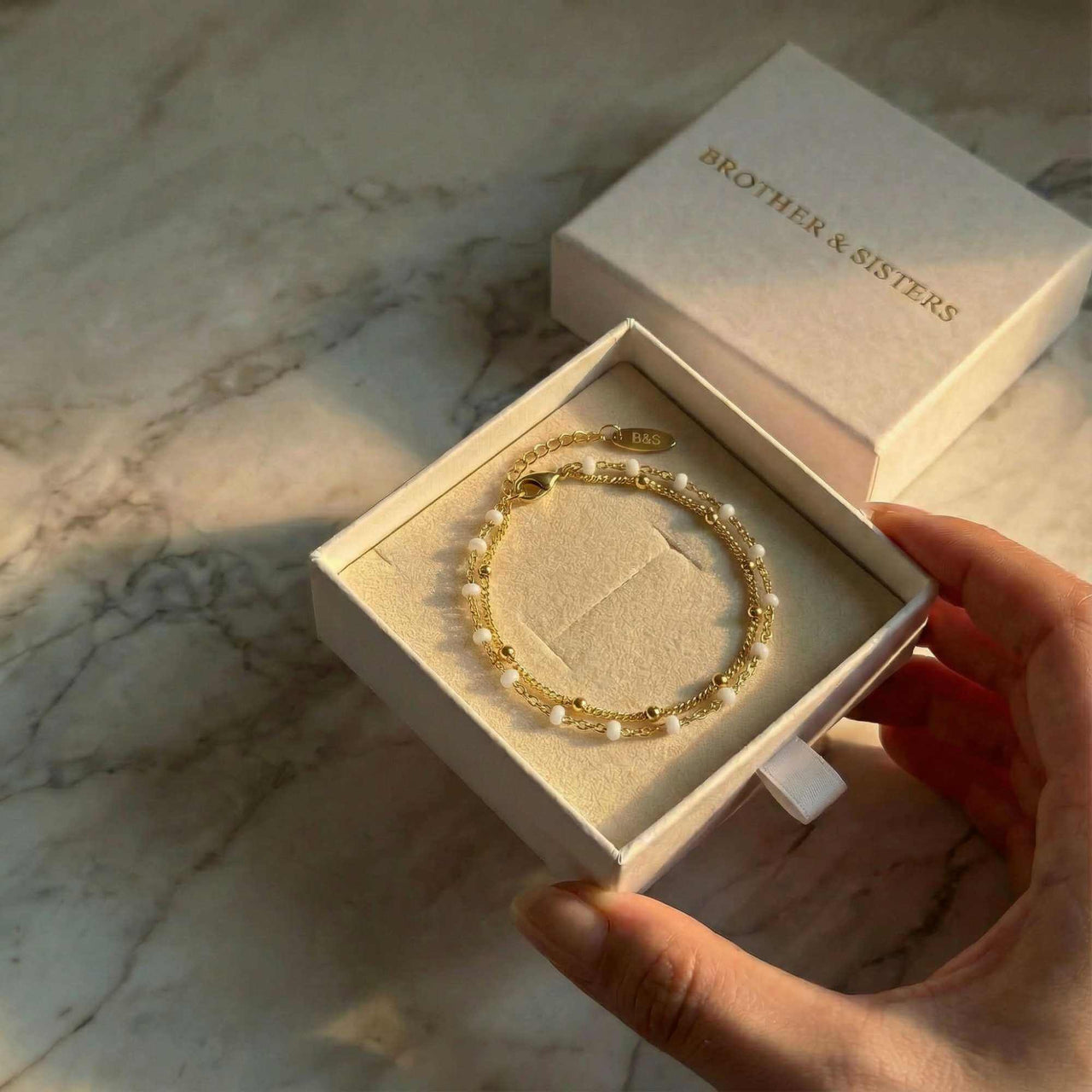 Double White Bracelet displayed in a box by Brother & Sisters, featuring white enamel beads and gold links.