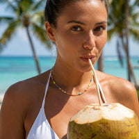 Thumbnail for A woman enjoying a coconut drink while wearing a Rainbow Choker by Brother & Sisters on a beach.