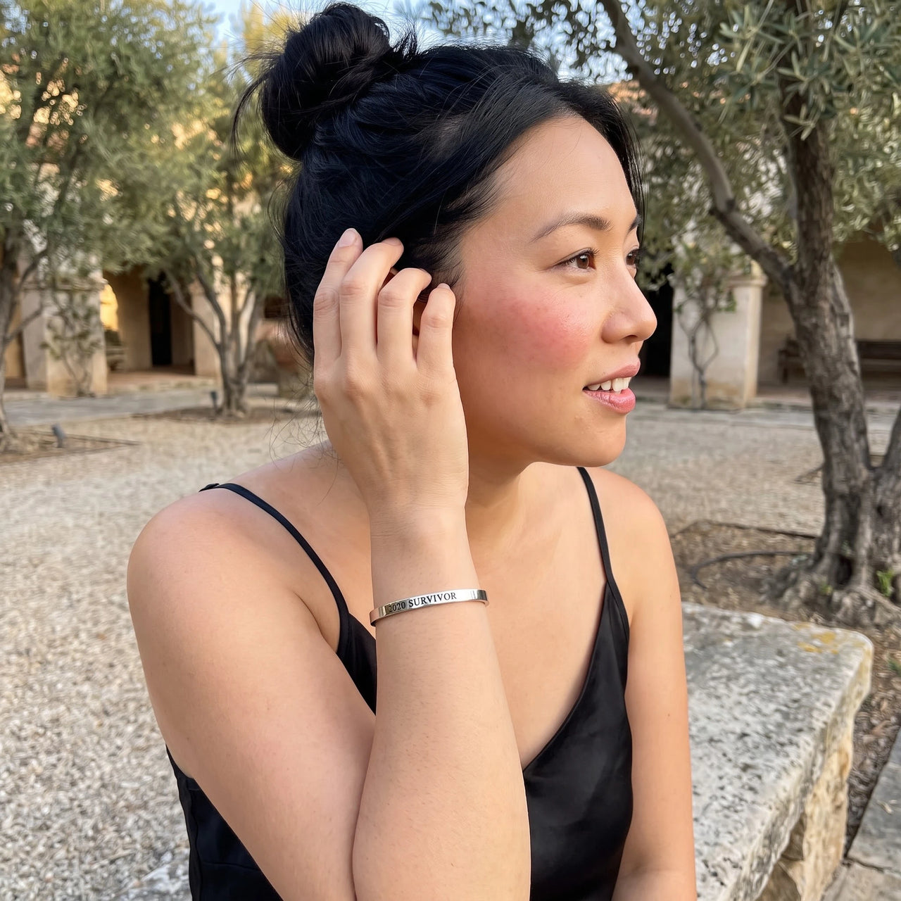 Woman gently touching her 2020 Survivor bracelet in silver | SKU: 2020s-wg