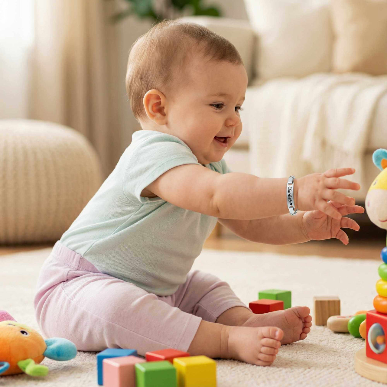 Infant Bracelet on baby playing with colorful toys, showcasing personalized charm by Brother & Sisters.