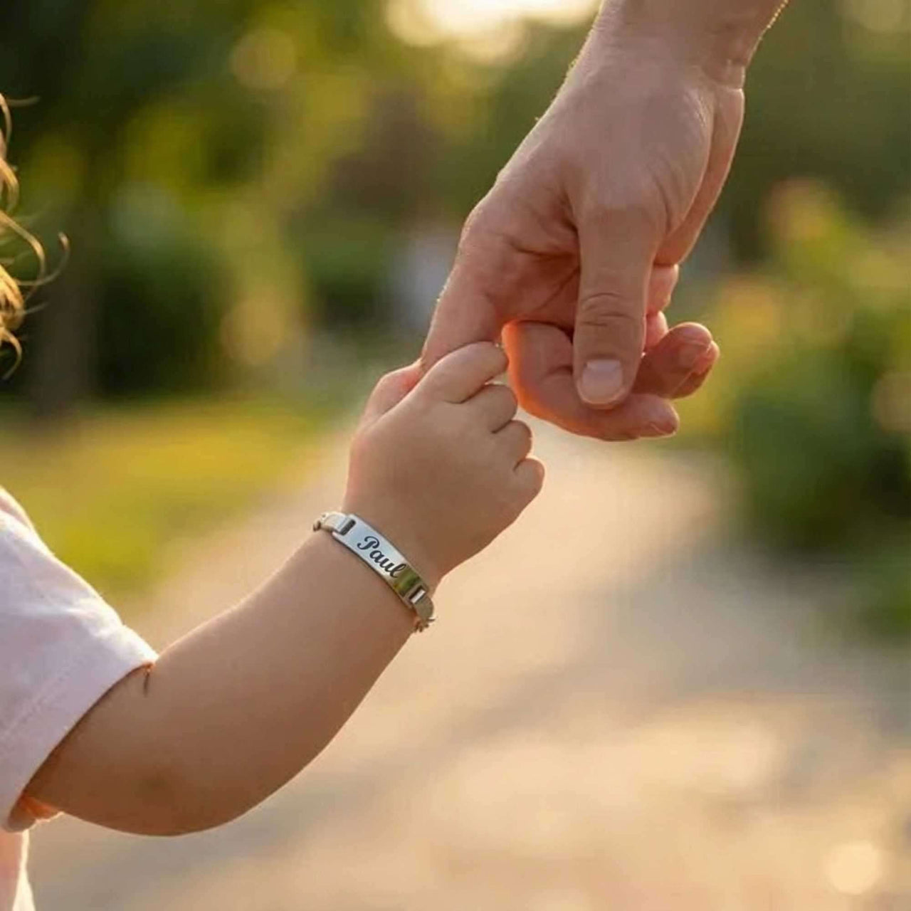 Infant Bracelet personalized with a child's name, held by an adult hand, from Brother & Sisters.