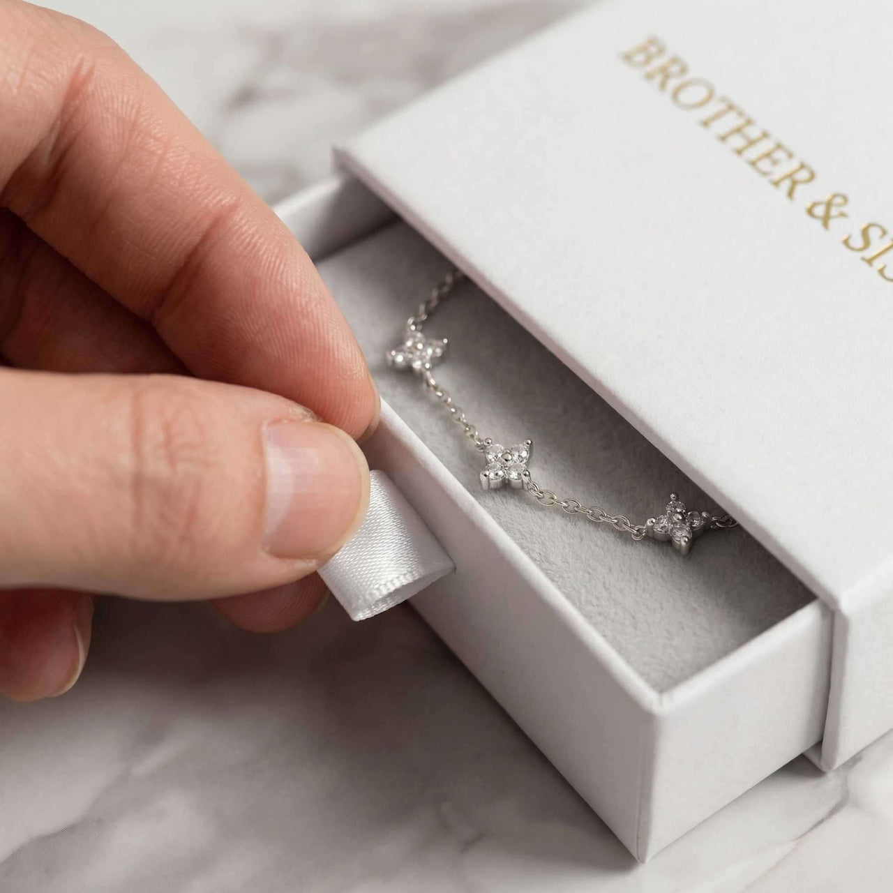 Hand holding a Crystal Flower Bracelet from Brother & Sisters, beautifully displayed in a white gift box.