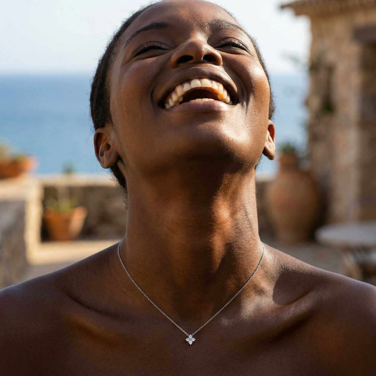 Woman smiling while wearing Crystal Flower necklace by Brother & Sisters — dainty refined four-leaf signature
