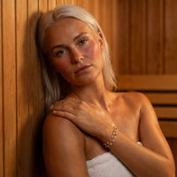 Thumbnail for Double White Bracelet worn by a model with pale skin in a wooden sauna, showcasing its elegant design from Brother & Sisters.