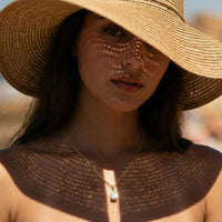 Thumbnail for Astra Teardrop Necklace featuring a shimmering teardrop-cut stone worn by a model in a sun hat.