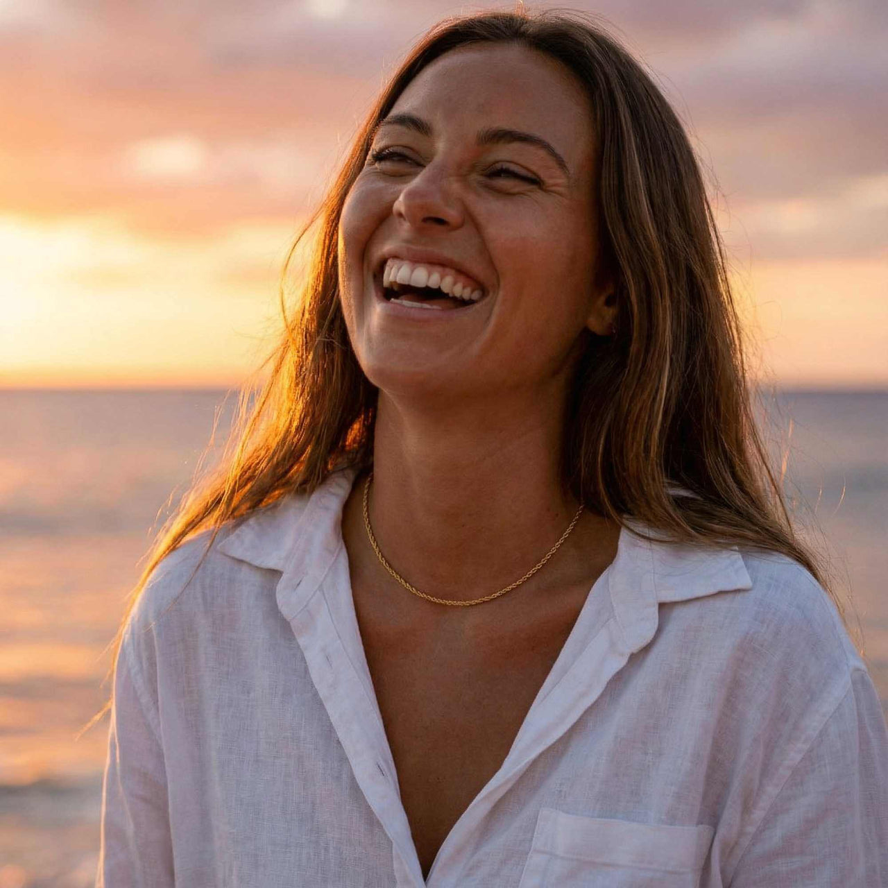 Woman smiling by the ocean wearing a Rope Chain Necklace, enjoying sunset, showcasing effortless style from Brother & Sisters.