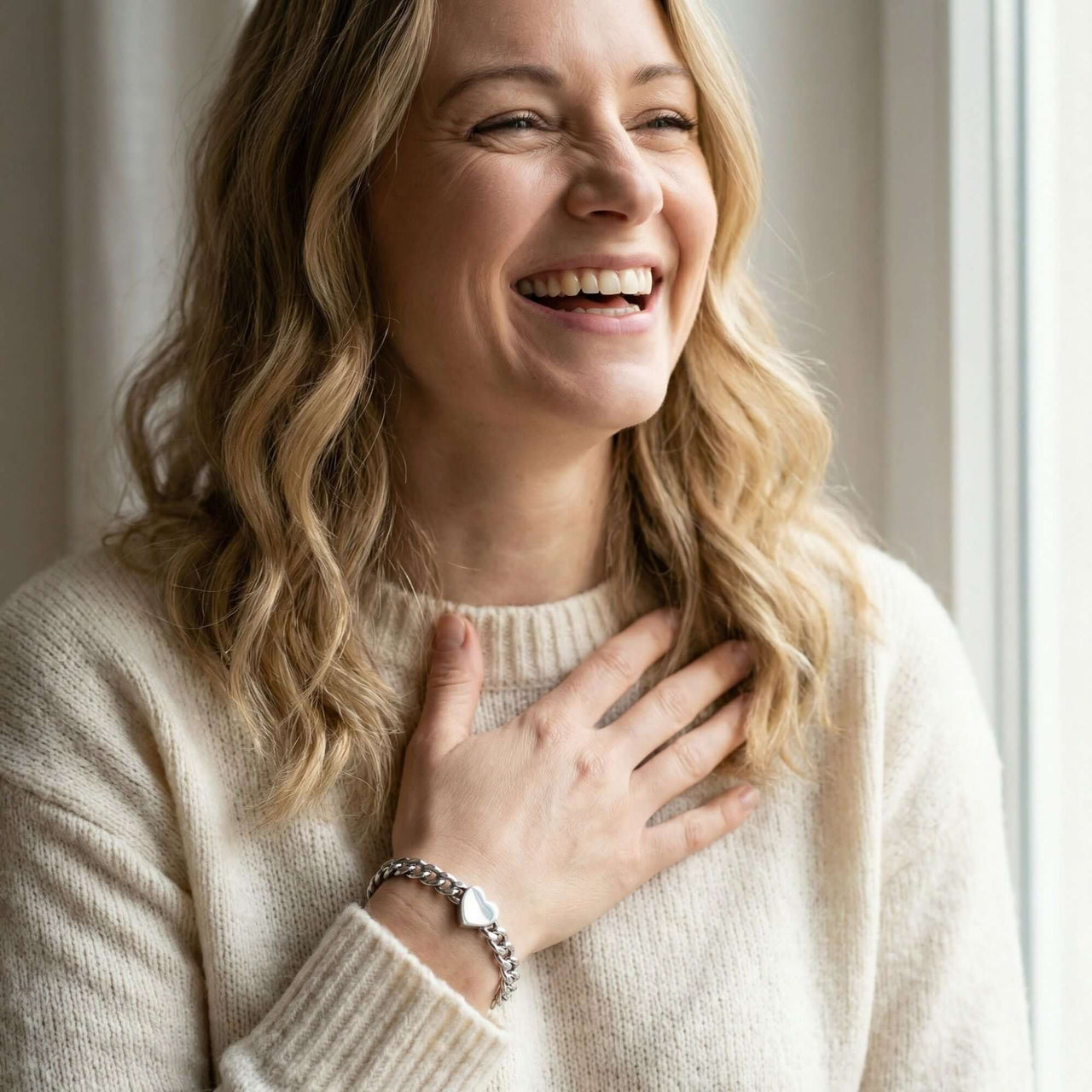 A woman smiling while wearing a Love Couple Bracelet by Brother & Sisters, showcasing the polished heart on a Cuban link chain.