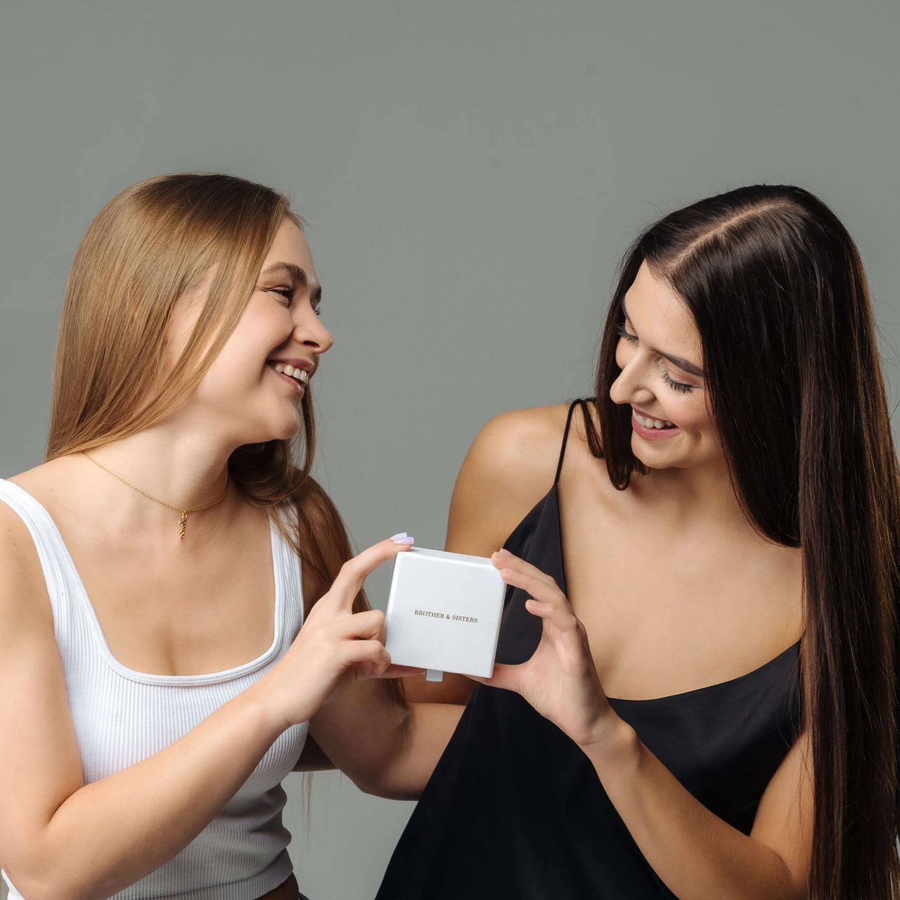 Two women joyfully presenting a gift box containing a Birth Flower Name Necklace from Brother & Sisters.