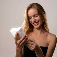 Thumbnail for Smiling woman holding a white gift box, excited about the Love Photo Necklace by Brother & Sisters.
