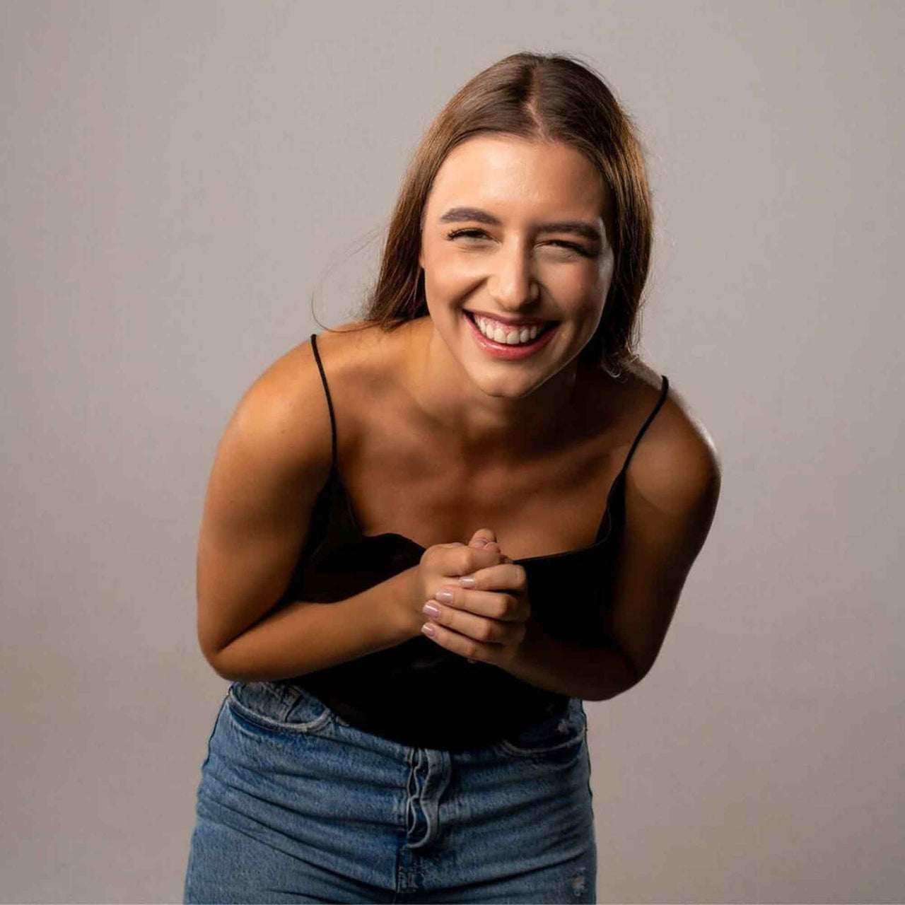 Smiling young woman wearing a black top and blue jeans, exuding joy and happiness.