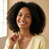 Thumbnail for Daisy Name Necklace worn by a smiling woman, featuring connected hearts and a white enamel daisy. Crafted by Brother & Sisters.