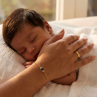Thumbnail for A close-up of a person's hand wearing a Photo Projection Bracelet by Brother & Sisters, with a sleeping baby nearby.
