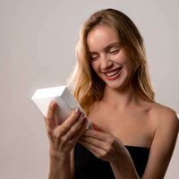 Thumbnail for Smiling woman holding a gift box, excited to open the Photo Projection Bracelet by Brother & Sisters.