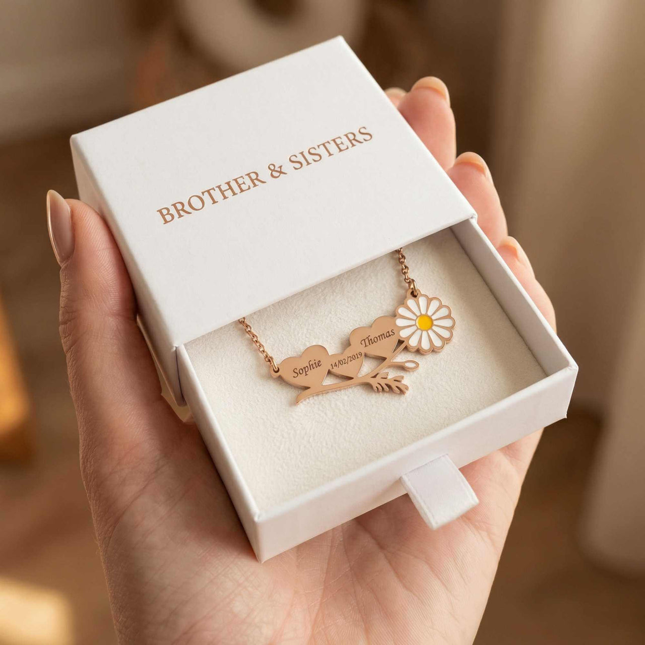 Daisy Name Necklace in a gift box from Brother & Sisters, featuring engraved names and a delicate white enamel daisy.