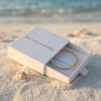 Thumbnail for Oval Bead Anklet by Brother & Sisters in a box on the beach, showcasing gold beads and luxury packaging.