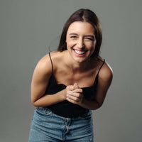 Thumbnail for Smiling woman in a black top and jeans, radiating joy and happiness, with a grey background.