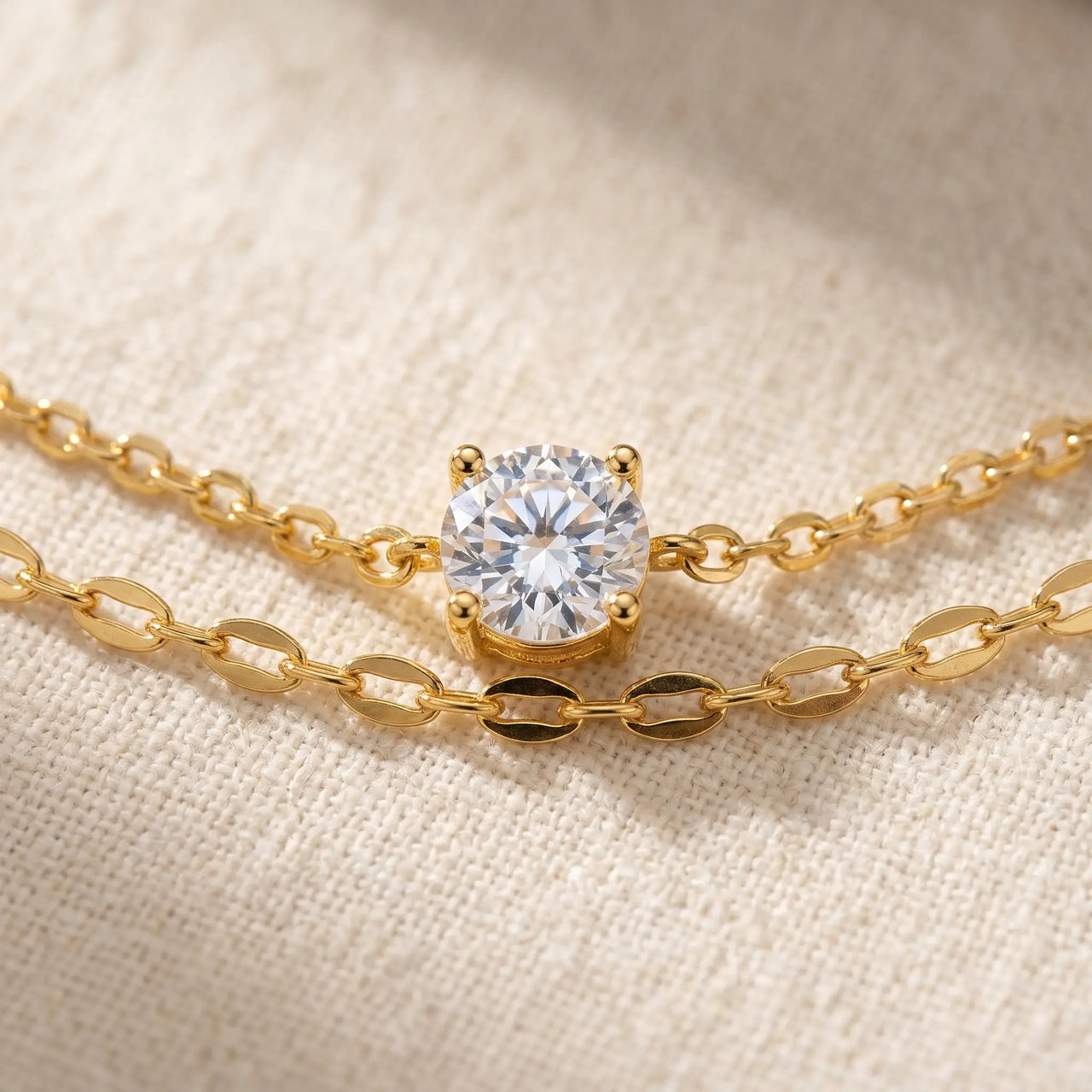 Amalfi Layered Anklet CZ solitaire macro — round crystal in 4-prong gold claw setting between cable and marquise chains on cream linen, sparkling diamond-like center