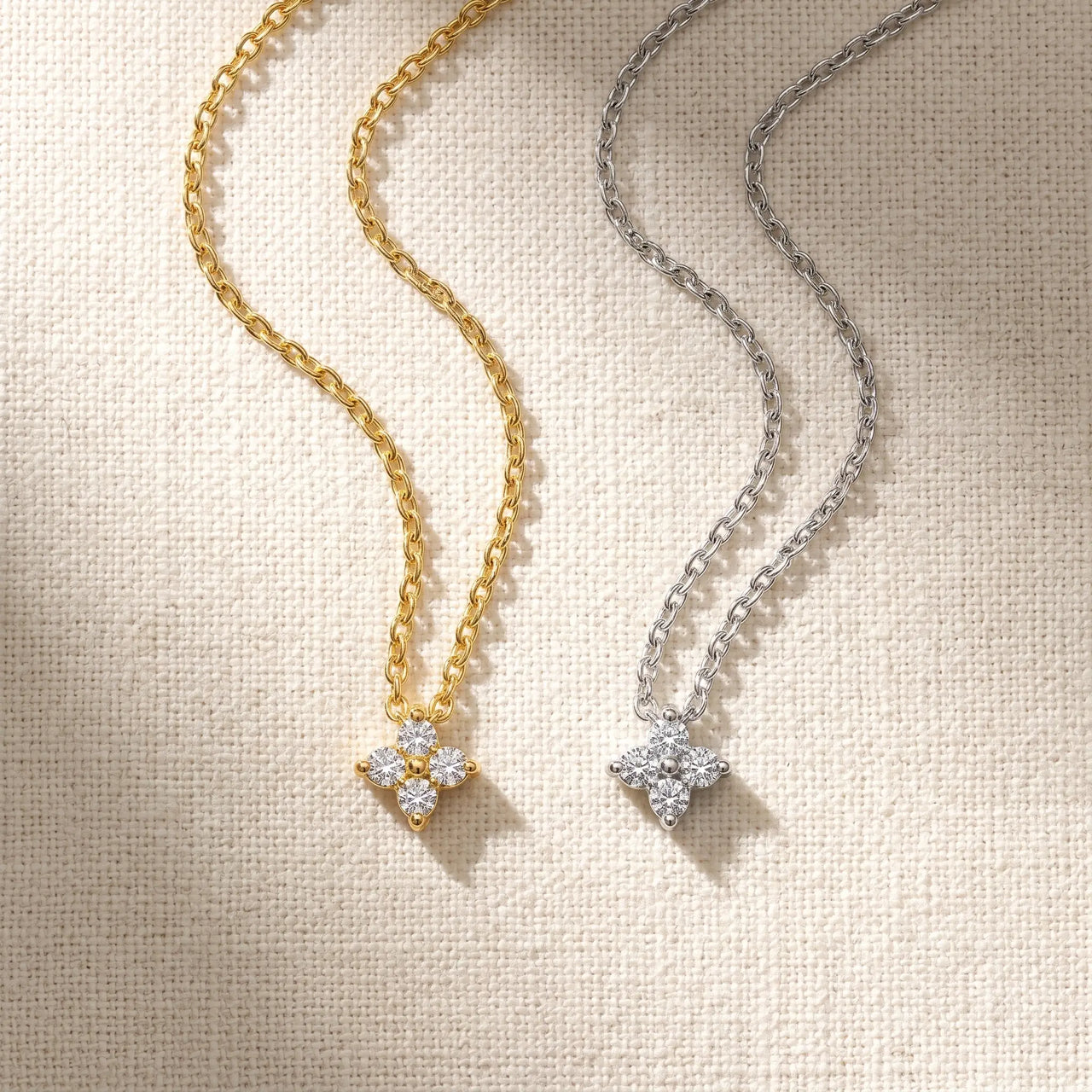 Crystal Flower necklace gold and silver side-by-side flatlay on cream linen — both finishes available, refined four-leaf zircon flower pendant