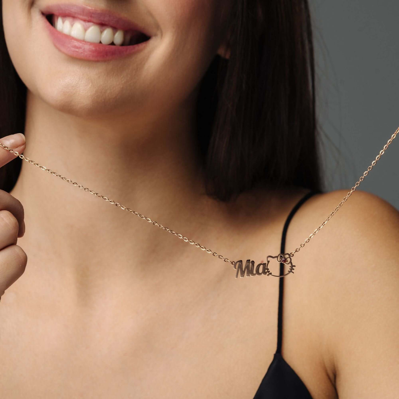 A woman showcasing the Kitty Name Necklace with her name 'Mia' in stylish font, from Brother & Sisters.