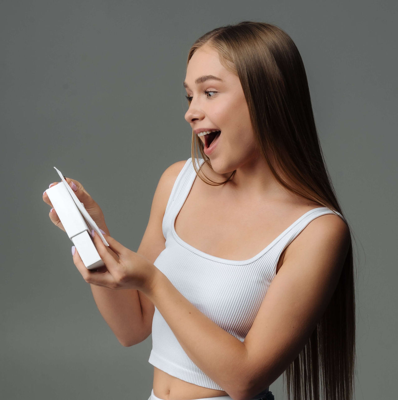 Young woman excitedly unwrapping a gift, showcasing the joy of receiving personalized jewelry.