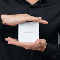 Thumbnail for Gold Cube Initial Necklace packaging held by hands from Brother & Sisters, showcasing stylish and meaningful jewelry.