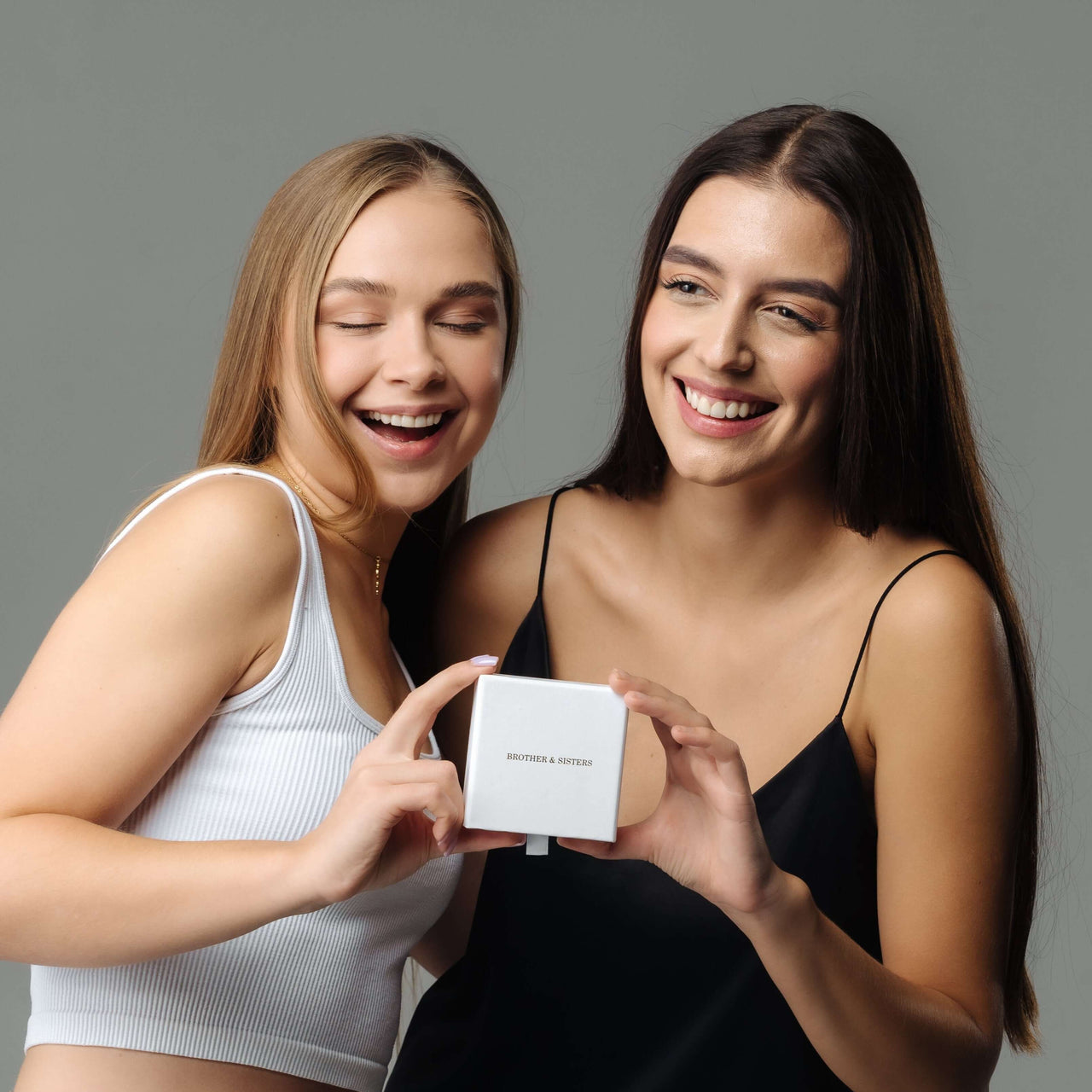 Two women joyfully showcasing a Minimalist Name Necklace box by Brother & Sisters, highlighting personalized elegance.