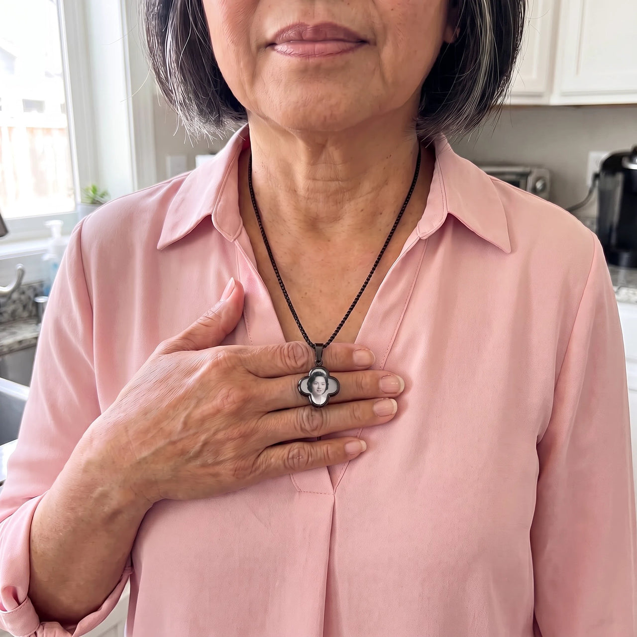 Woman in a pink blouse warming the black clover pendant with her thumb to reveal the photo | SKU: TPH-CLVN-BLACK