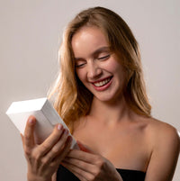 Thumbnail for Smiling woman opening a gift box, excited about the Timeless Photo Necklace by Brother & Sisters.