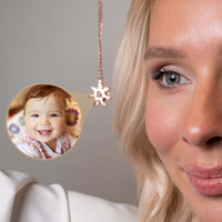 Thumbnail for Close-up of a woman wearing a Sun Photo Necklace by Brother & Sisters, featuring a smiling baby photo illuminated by light.
