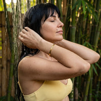 Thumbnail for Travel To Feel Alive bracelet in gold worn in an outdoor shower | SKU: ttfa-g