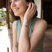 Thumbnail for Woman gently touching her Travel To Feel Alive bracelet in silver | SKU: ttfa-wg